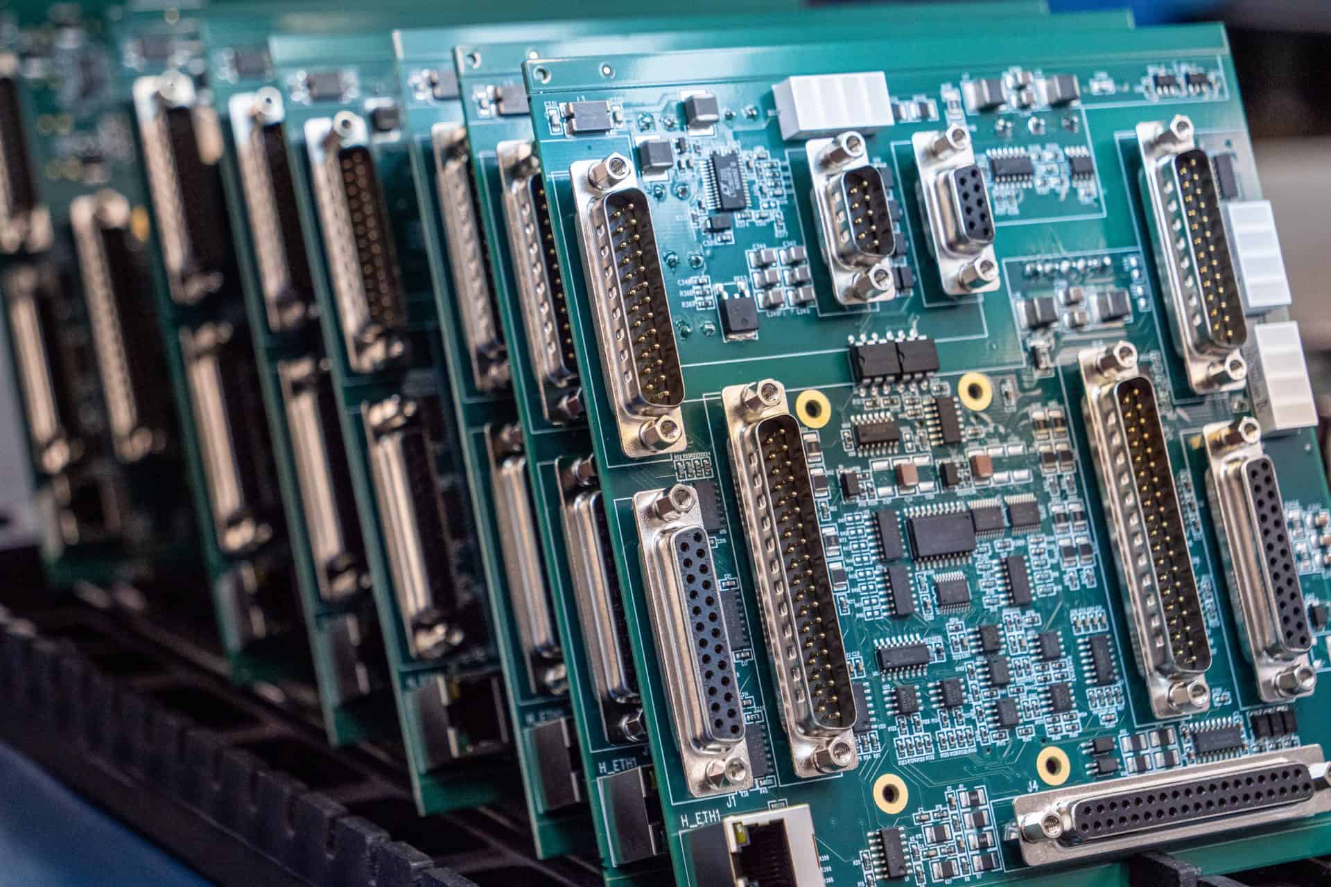A row of green circuit boards with multiple connectors and electronic components are lined up in a tray.